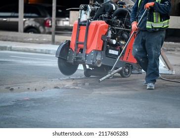 Worker using an asphalt saw cutting machine to excavate street and worker with broom