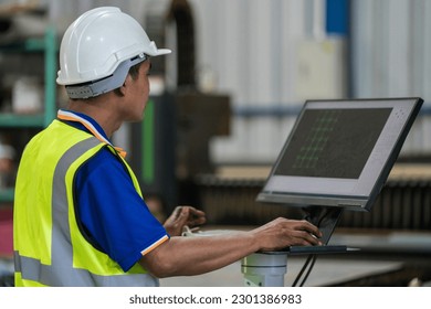 A worker is using a computer to control a steel laser cutting machine in a factory.