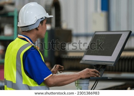 A worker is using a computer to control a steel laser cutting machine in a factory.