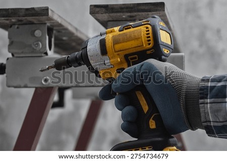Worker using cordless impact driver to fasten metal structure. Professional installation process at construction site. Concept of industrial work, renovation, engineering and building assembly
