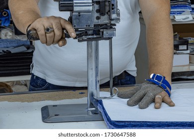 Worker using a cutter - a large machine for cutting fabrics -  in a textile factory, he wears a chain glove.