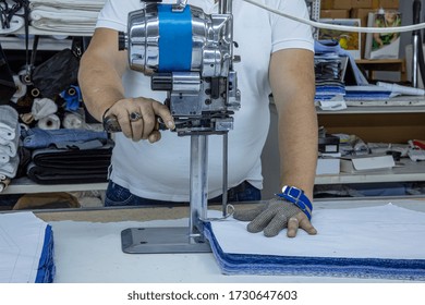Worker using a cutter - a large machine for cutting fabrics -  in a textile factory, he wears a chain glove.