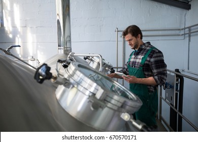 Worker using digital tablet while examining vat at factory - Powered by Shutterstock