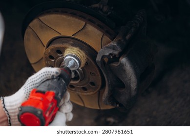 Worker using a drill with a wire brush attachment to clean rust from a car brake disk during vehicle maintenance