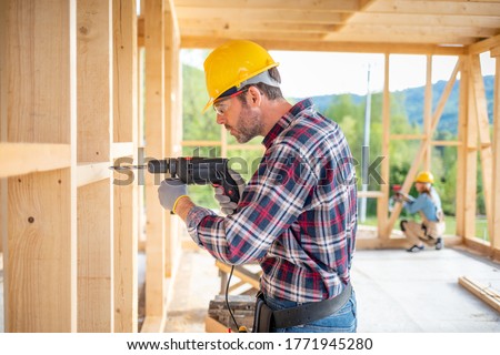Worker using drill working on construction of wood frame house