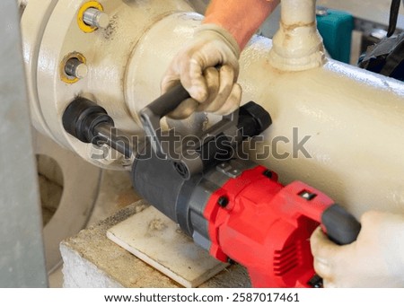 Worker using an electric impact wrench to dismantle a pipeline flange connection.