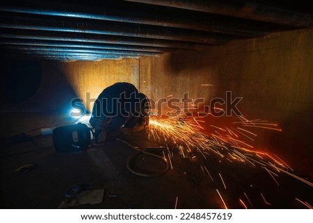 Worker using electric wheel spark grinding metal is part of machinery plate tank beam pipe construction flash spark inside confined spaces.