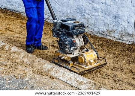 Worker using gas-powered compactor to compact sand on verge before paving