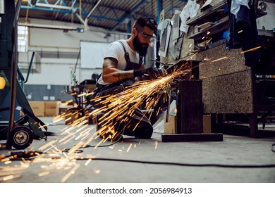 A worker using the grinder for metal processing while crouching in his workshop. Small business worker, blue-collar worker. Worker in workshop