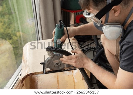 Worker using handheld circular saw on wooden board indoors.