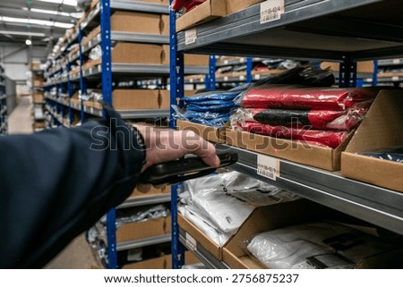 Worker using a handheld scanner to scan a barcode in a warehouse aisle, managing inventory and stock levels in a distribution centre