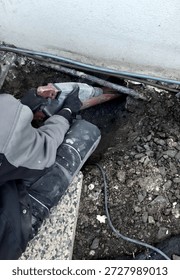 worker is using heavy hammer drill or jackhammer, excavate, drill into ground, masonry below ground level. work is taking place in close proximity to perimeter wall of house, installing new utilities, repairing waterproofing