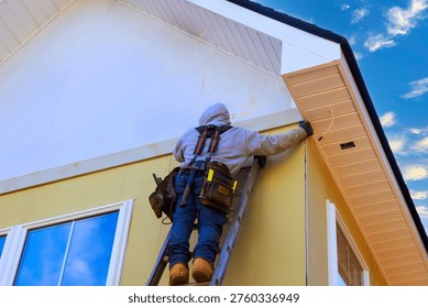 Worker is using ladder to fix trim on house while installing fiber siding panels