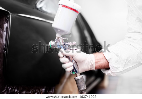Worker using a\
paint spray gun for painting a\
car