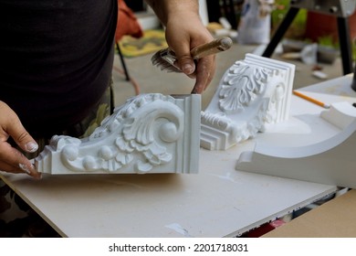The worker is using a paintbrush to that are paint wooden corbels for the kitchen island