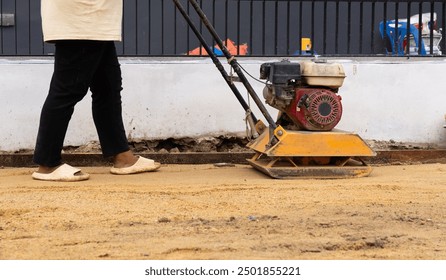 Worker Using Plate Compactot to Compact Sand for Paver. Construction Concept