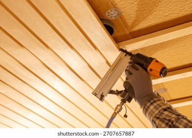 Worker using pneumatic nail gun to secure wooden ceiling panels during interior renovation, timber construction process, insulation layers, manual labour, craftsmanship and precise home improvement