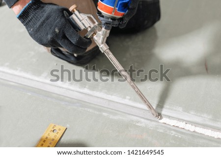 Worker is using a polyurethane foam for gluing drywall at ninety degrees. Hand holding polyurethane expanding foam glue gun applicator