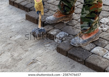 Worker using rubber mallet to set cobblestones, close-up of feet and hands on paving work.