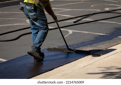 Worker using a sealcoating brush during asphalt resurfacing project  - Shutterstock ID 2214765009