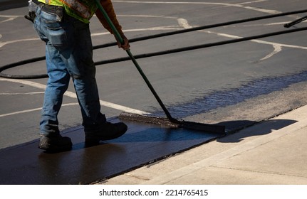 Worker using a sealcoating brush during asphalt resurfacing project  - Shutterstock ID 2214765415
