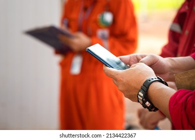 A worker is using smartphone to searching some information during safety meeting with other colleague (as blurred background). Industrial worker action photo. Close-up and selective focus at hand. - Powered by Shutterstock