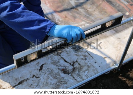 Worker using a spirit level on a greenhouse frame. Greenhouse from an English allotment.