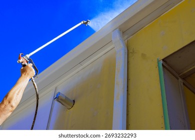 Worker is using spray gun to apply paint to exterior of house