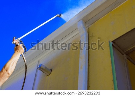 Worker is using spray gun to apply paint to exterior of house