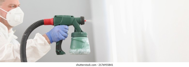 Worker using spray gun for coloring wall in white. Effective and fast way to paint wall