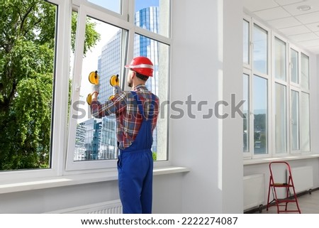Worker using suction lifters during plastic window installation indoors