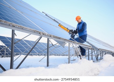 Worker using tools on solar panels covered in snow, performing maintenance at a renewable energy farm during winter