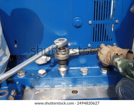 Worker using a torque wrench to tighten bolts on an industrial blue machine. The image highlights the precision and strength required in industrial assembly and maintenance tasks.
