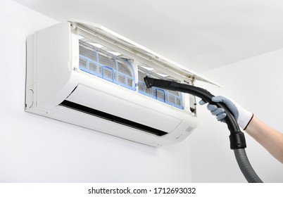 A worker is using a vacuum cleaner to clean the air conditioner.Air conditioner system on white wall room. Air conditioning.A white air conditioner is installed on a white wall in the apartment.
 - Shutterstock ID 1712693032