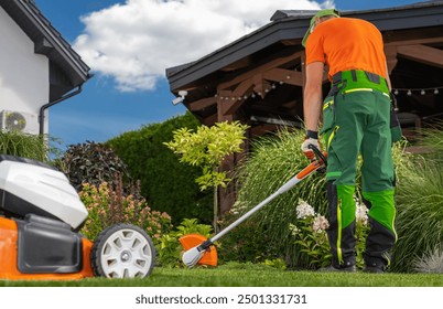 A worker in vibrant attire uses a string trimmer to maintain the lush garden, surrounded by colorful plants under a clear blue sky.