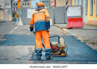 Worker With Vibratory Plate Compactor For Road Construction. Road Repair, Worker Paving Fresh Bitumen. Pothole Repair, Asphalt Paving, Patching Road Works With Plate Compactor.