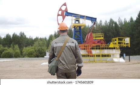 Worker Walking To Oil Pump Jacks In Oilfield. Balancing Drive Rod Pumps Oil Rocker. Pumping Crude Oil For Fossil Fuel Energy With Drilling Rig In Oil Field.