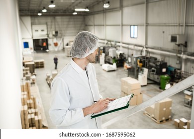 Worker In Warehouse For Food Packaging. Manager Writing On Clipboard In Automated Production Line At Modern Factory. View From Above. Color Toned Image.