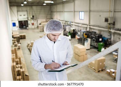 Worker In Warehouse For Food Packaging. Manager Writing On Clipboard In Automated Production Line At Modern Factory. View From Above. Color Toned Image.