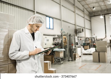 Worker In Warehouse For Food Packaging. Manager Writing On Clipboard In Automated Production Line At Modern Factory. Color Toned Image.