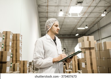 Worker In Warehouse For Food Packaging. Manager Writing On Clipboard In Automated Production Line At Modern Factory. Color Toned Image.