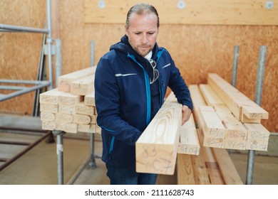 Worker In A Warehouse, Lumber Mill Or Woodworking Factory Selecting A Large Wooden Beam Off A Storage Rack To Use In Production