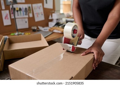 Worker of warehouse sealing packed cardboard box with order with cellotape