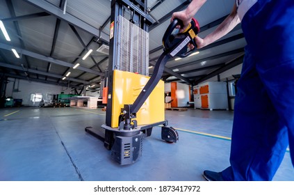 A worker in a warehouse uses a hand pallet stacker to transport pallets. - Powered by Shutterstock