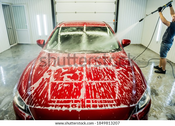 Worker washing car with high pressure water at a\
car wash.