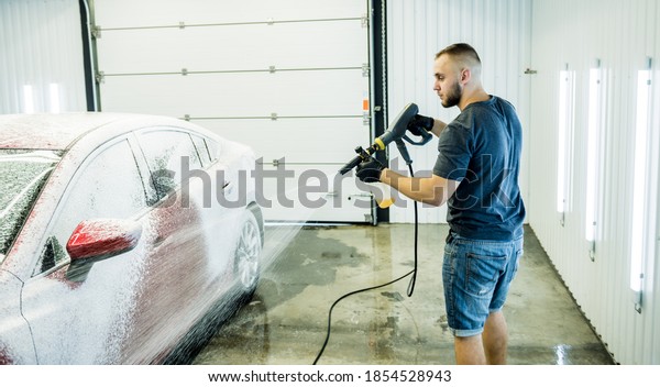 Worker washing car with high pressure water at a\
car wash.