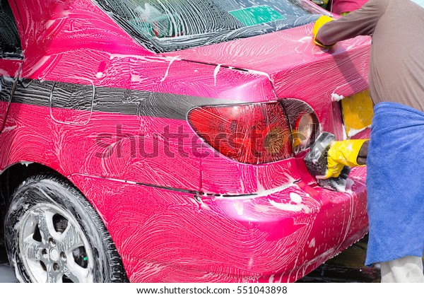 A worker washing pink and\
black taxi car with soap or foam, and wear protective gloves while\
working