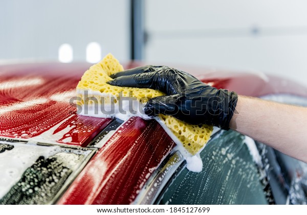 Worker washing\
red car with sponge on a car\
wash