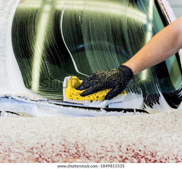 Worker washing\
red car with sponge on a car\
wash