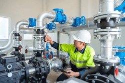A Worker At A Water Supply Station Inspects Water Pump Valves Equipment In A Substation For The Distribution Of Clean Water At A Large Industrial Estate. Water Pipes. Industrial Plumbing.